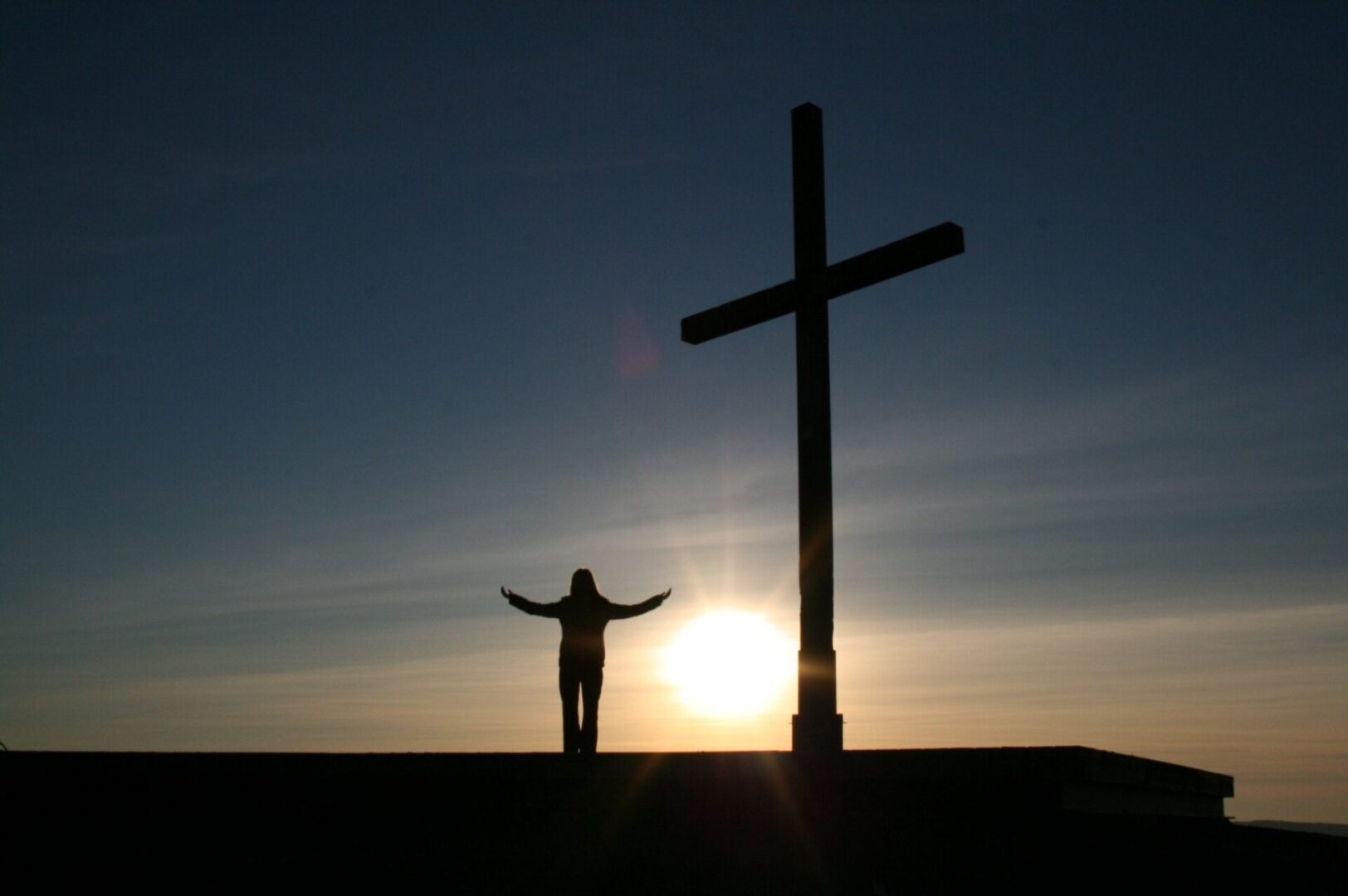 A silhouette of a person standing on top of a cross.